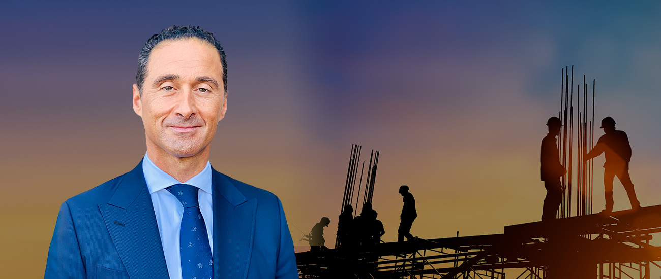 Bruce Kokozian with a construction site in the background at sunset, showing silhouetted workers and scaffolding.